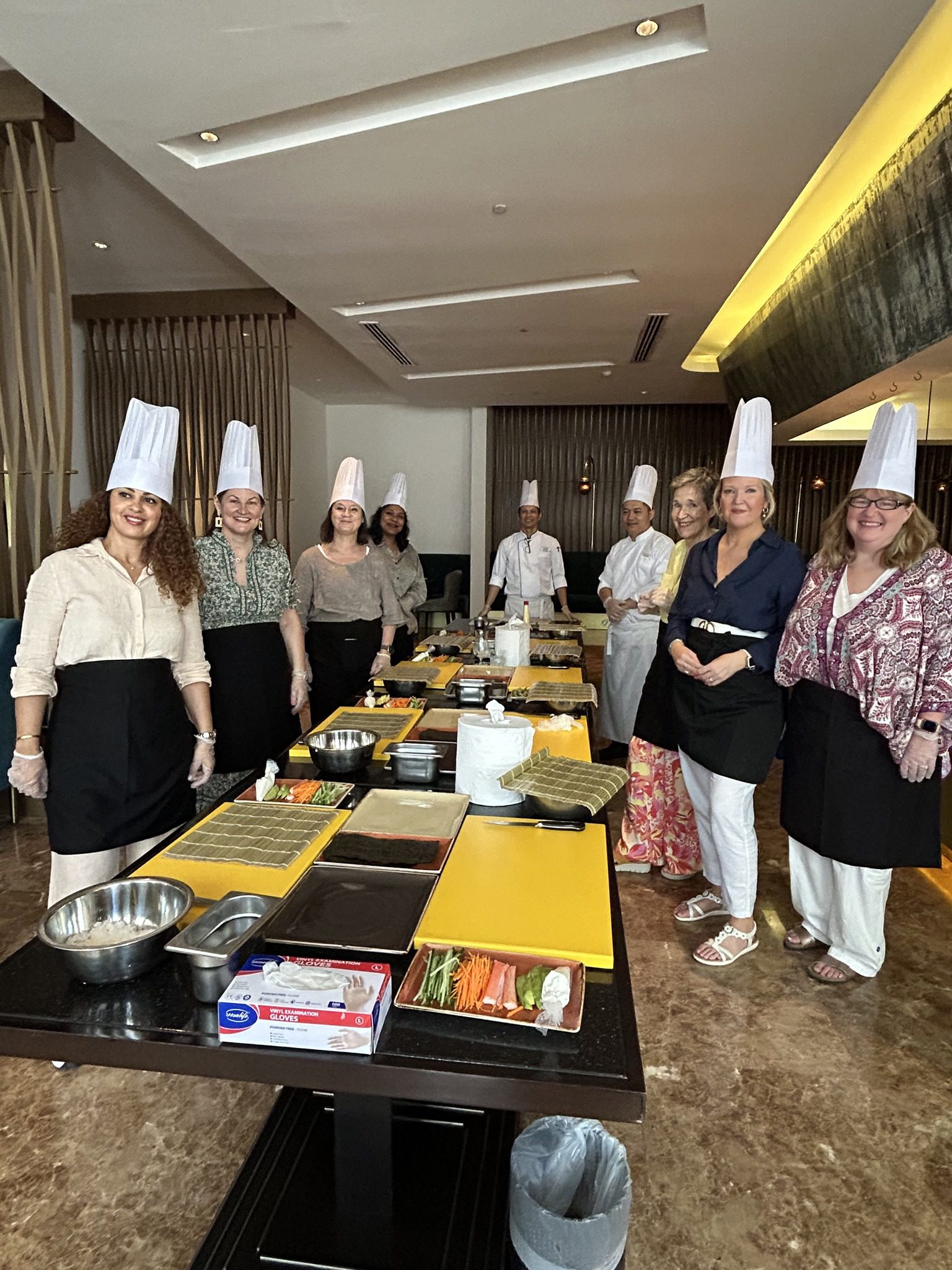 7 WGO female members standing with white chef hats on around a table taking a cooking class