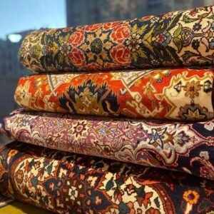 Stack of rolled handmade Iranian Persian carpets with floral and geometric patterns in reds, navies, and creams, at Al Besat Carpets, Al Khuwair, Muscat