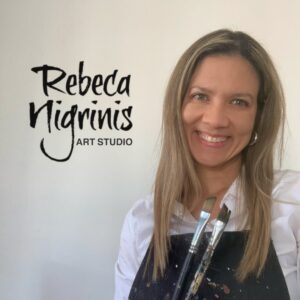 Rebeca Nigrinis, Colombian contemporary artist based in Muscat, holding paintbrushes in her Qurum art studio