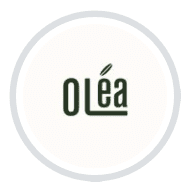 Circular cream logo for Olea Restaurant with dark green lettering and a small leaf detail, at Voco Hotel, Al Mouj, Muscat